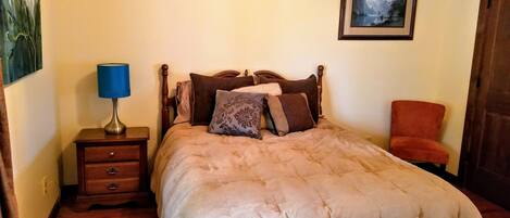 Une chambre à coucher avec un lit, une table de chevet, une lampe, une chaise et un tableau encadré au mur.