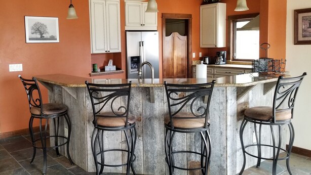 Una cocina con una isla central, taburetes de bar y un refrigerador.
