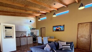 A spacious living area with a blue sofa, a dining table, and a kitchen in the background. - Peumayen Atacama / Hostal & Cabaña (San Pedro de Atacama)