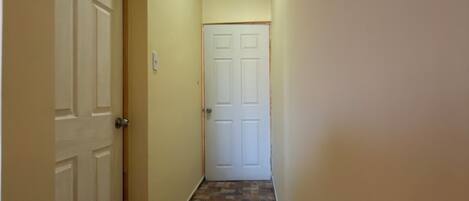 A narrow hallway with patterned flooring, two white doors, and a ceiling with recessed lighting.