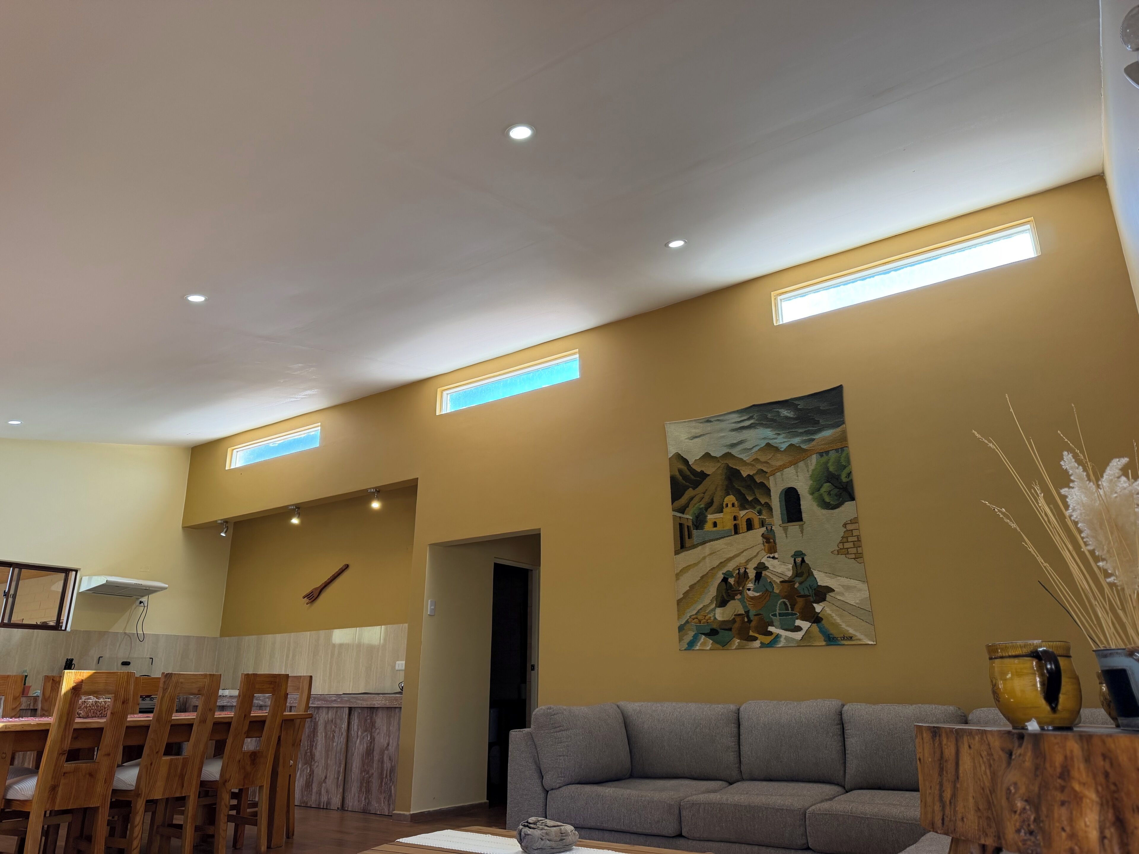A dining area with wooden chairs and a table, a gray sofa, and a painting on the wall.