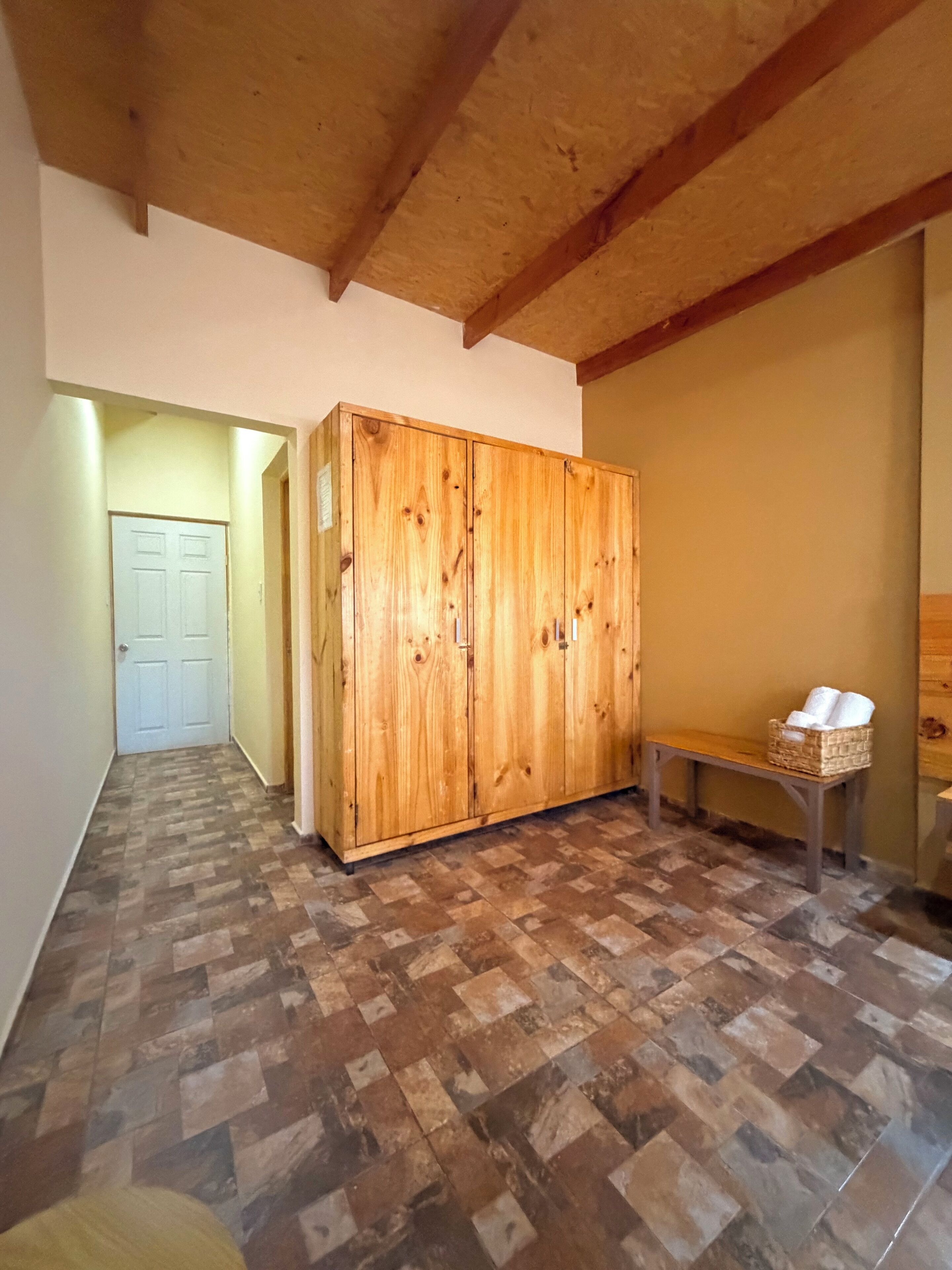 Um corredor com um guarda-roupa de madeira, um banco com uma cesta e uma porta no final.