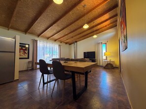 Een eetgedeelte met een houten tafel en stoelen, een televisie en een schilderij aan de muur.