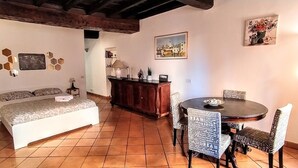 Una habitación acogedora con una cama, una mesa de comedor con sillas, un armario de madera y un cuadro en la pared.