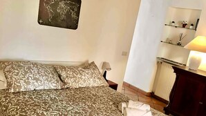Una cama bien hecha con una colcha estampada, una mesita de noche con lámpara y un mapa del mundo en la pared.