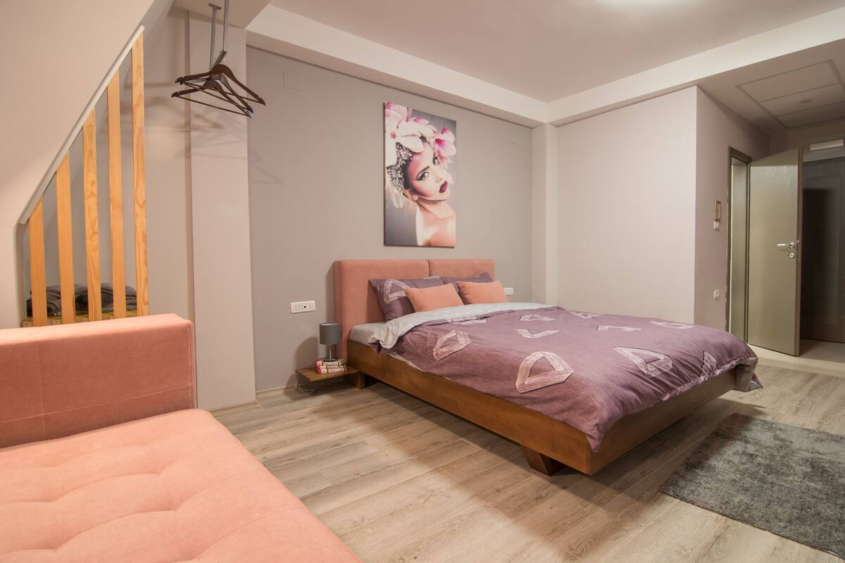 Un dormitori modern amb un llit, una petita taula de nit, una cadira i una escala.