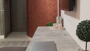 A modern kitchen with a large copper-colored cylindrical column, a grey countertop with a laptop, and small potted plants. - Vanilla Boutique Hotel (Skopje)