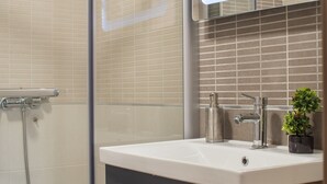 A modern bathroom with a glass shower enclosure, a sink with a mirror, and a small potted plant. - Vanilla Boutique Hotel (Skopje)