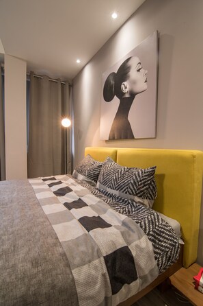 A modern bedroom with a bed, a yellow headboard, and a wall-mounted artwork.