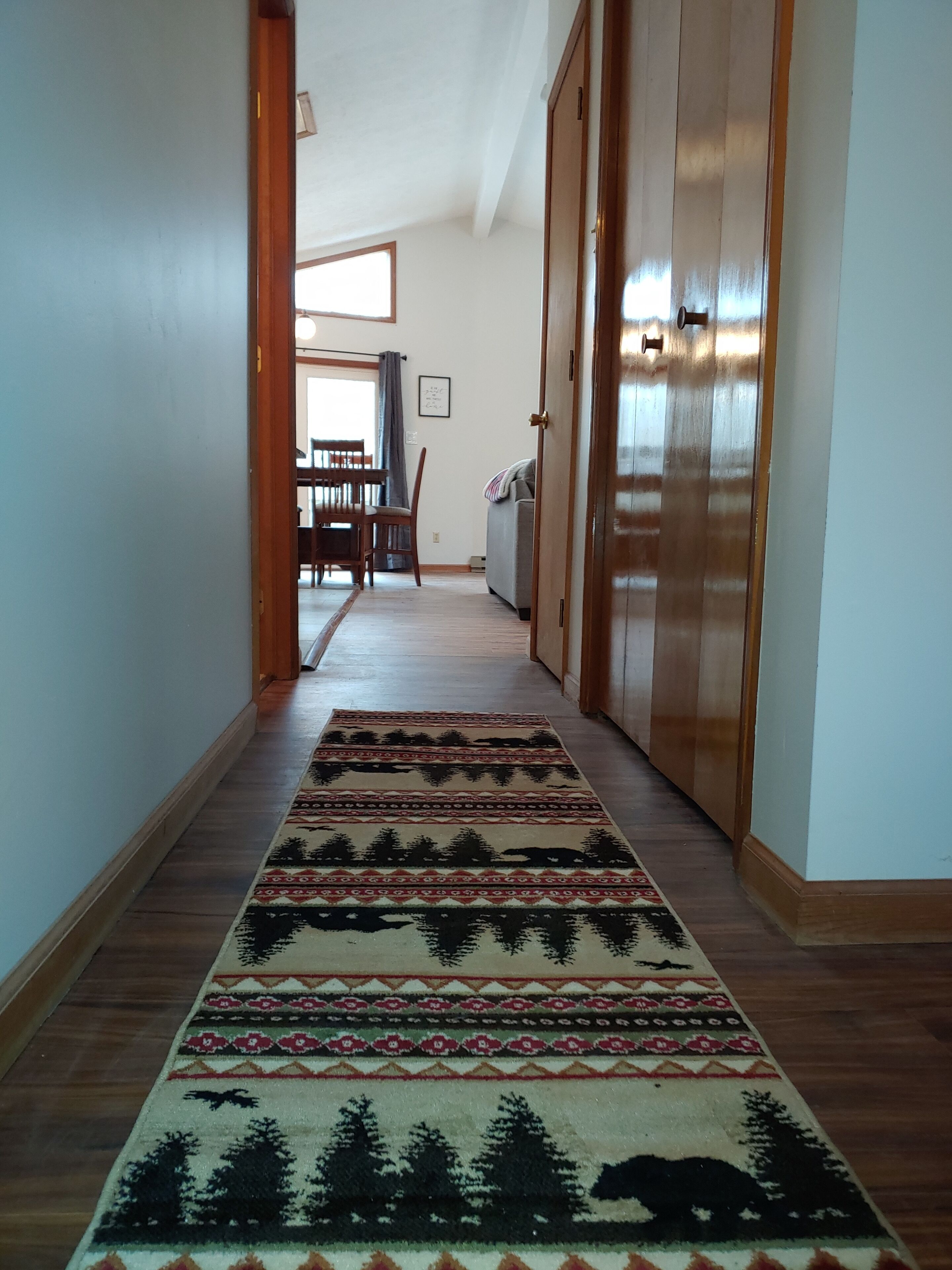 Un couloir avec un tapis à motifs, des portes en bois et, au fond, un coin repas.