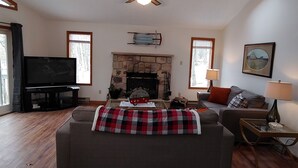 A living room with a fireplace, a television, and a ceiling fan.