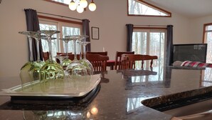 A kitchen with a marble countertop, wine glasses, and a dining area with wooden chairs and a table.
