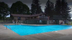 A swimming pool with a wooden building in the background, surrounded by trees.