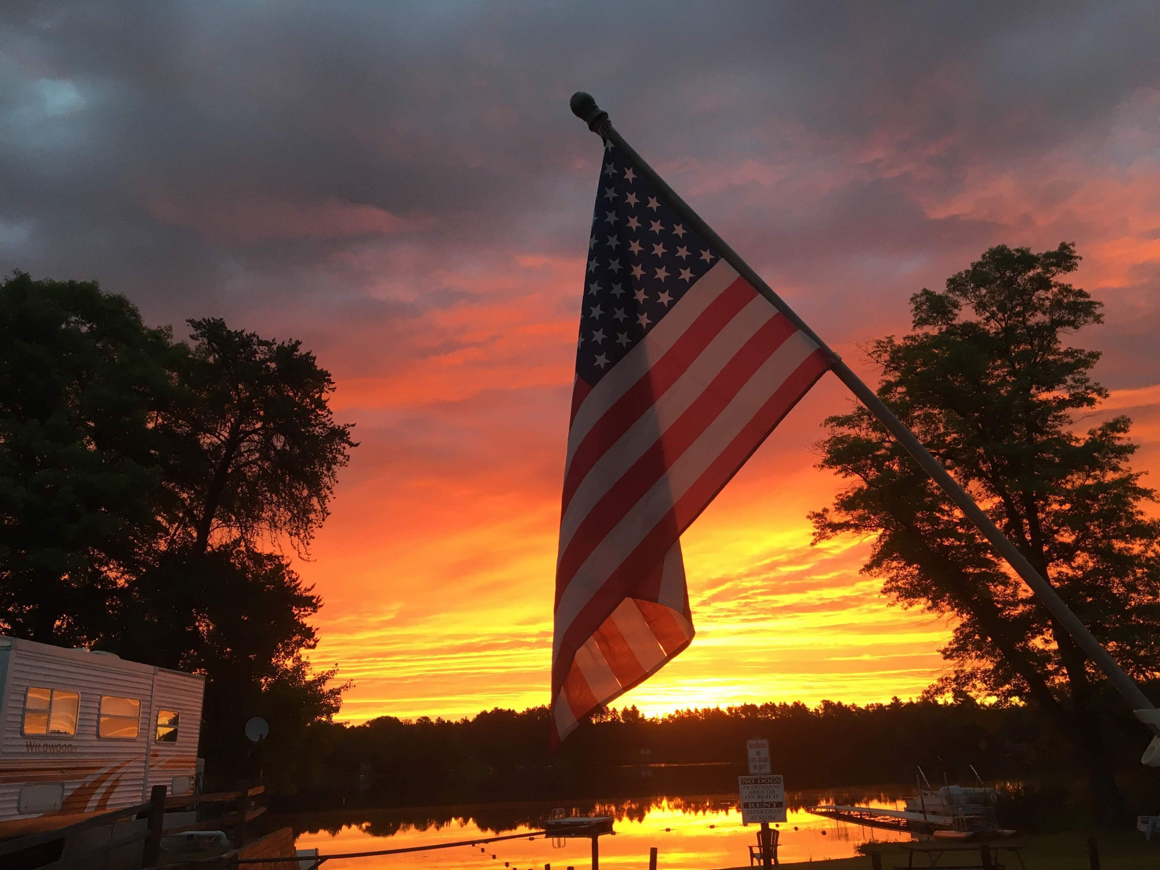 En amerikansk flagga på en flaggstång med en solnedgång i bakgrunden.