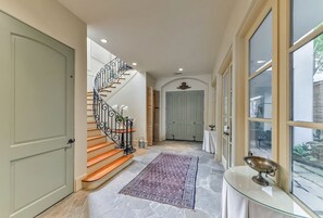 A grand hallway with a marble floor, a decorative rug, a glass table with a metal bowl, and a spiral staircase with a metal railing.