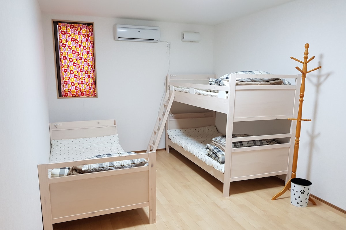 A bunk bed with a ladder, a single bed, and a coat rack in a room with wooden flooring and white walls.