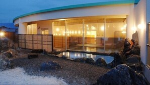 Um edifício moderno com um telhado curvo, amplas janelas de vidro e uma área de piscina com pedras e pedregulhos.