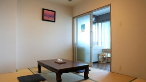 Um quarto com piso de tatame, uma mesa de madeira escura com um objeto pequeno sobre ela e um quadro na parede.