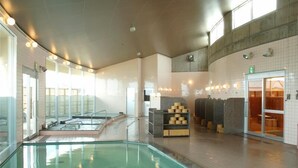 Área da piscina com barreira de vidro, sauna e sala de trocas com armários.