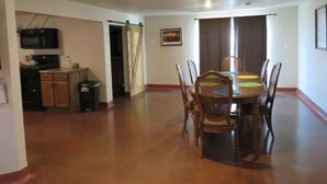 Een eethoek met een houten tafel en stoelen, een keuken met een magnetron, en een schuifdeur naar een andere kamer.