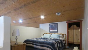 Een slaapkamer met een bed, een nachtkastje met een lamp, een houten kledingkast en een lijst met een afbeelding aan de muur.