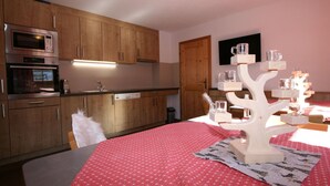 A modern kitchen with wooden cabinets, a microwave, and a dishwasher. There's a dining table with a red tablecloth and a white decorative tree centerpiece.