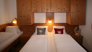 A room with two beds, wooden cabinets above, and wall-mounted lamps.