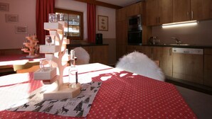 A cozy kitchen with wooden cabinets, a dining table with a red tablecloth, and a window with red curtains.