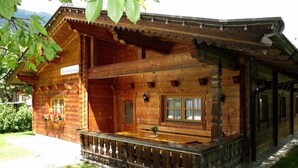 A wooden chalet with a balcony, a wooden porch, and a sign indicating it is a guesthouse.