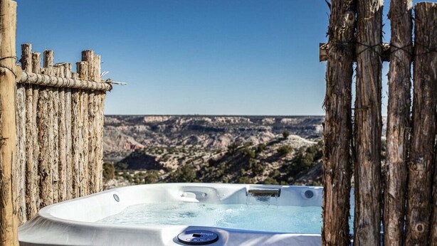 Ein Whirlpool mit Bedienfeld, umgeben von Holzzäunen, mit Blick auf eine gebirgige Landschaft.