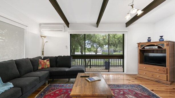 A living room with a dark sofa, a wooden coffee table, and a TV on a wooden cabinet. - The Beach Hive - Inlet Side Inverloch (INVERLOCH)