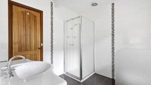 A bathroom with a wooden door, a glass shower enclosure, and a white sink. - The Beach Hive - Inlet Side Inverloch (INVERLOCH)