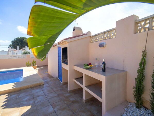 An outdoor patio with a pool, a barbecue area, and a table with a bottle and glasses. - Wonderful private villa for 11 guests with WIFI, A/C, private pool, TV, patio and pets allowed (Calpe)