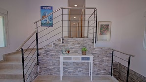Un escalier avec un mur en pierre, une console blanche ornée d’objets décoratifs et une affiche accrochée au mur.