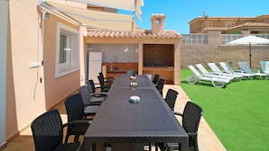 Un espace extérieur aménagé pour les repas, avec une longue table et des chaises, un barbecue intégré et un petit coin cuisine.