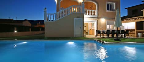 A two-story house with a swimming pool, a balcony, and a patio area with outdoor furniture.