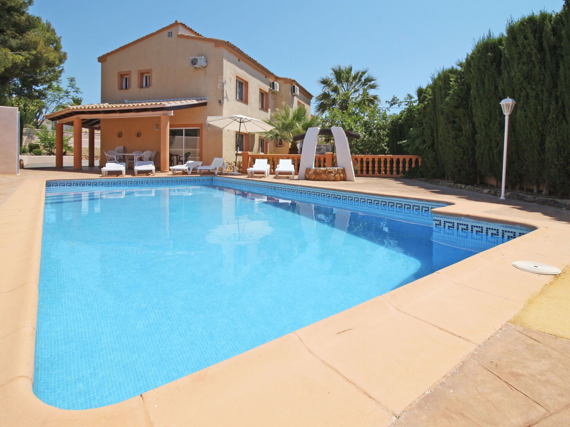 A swimming pool with lounge chairs and umbrellas, surrounded by a house and trees.
