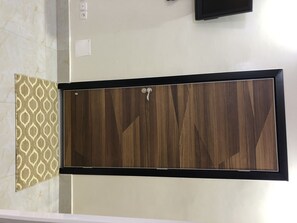 Une salle de bain avec un meuble-lavabo en bois, un tapis à motifs et un téléviseur fixé au mur.