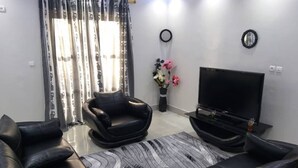 Una sala de estar moderna con un televisor de pantalla plana, dos sofás de cuero negro, un tapete estampado y un jarrón decorativo con flores.