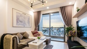 A modern living room with a sofa, coffee table, and a large window offering a city view. - Infinity Pool Signature - Saigon Rivergate (Ho Chi Minh City)