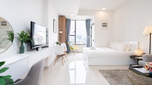 A modern hotel room with a large bed, a desk with a flat-screen TV, a dining area with chairs, and a view of the city through large windows. - Infinity Pool Signature - Saigon Rivergate (Ho Chi Minh City)