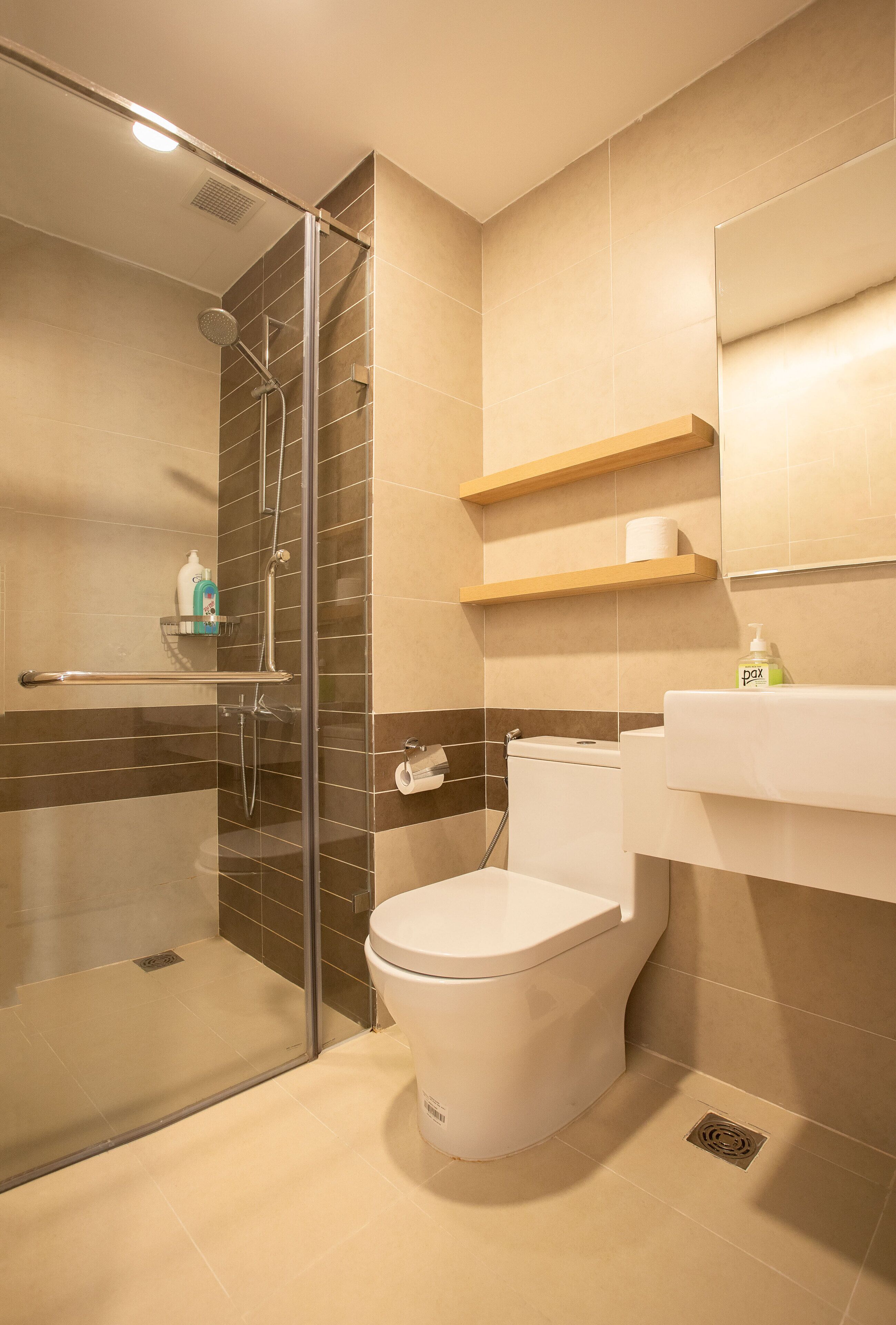 A modern bathroom with a glass-enclosed shower, a white toilet, and beige tiles.