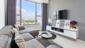 A modern living room with a large window, a sofa, a coffee table, and a TV on a white cabinet. - Infinity Pool Signature - Saigon Rivergate (Ho Chi Minh City)