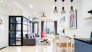 A modern living room with a grey sofa, a dining table with chairs, and a kitchen area with a blue cabinet. - Infinity Pool Signature - Saigon Rivergate (Ho Chi Minh City)