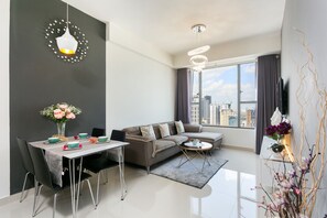 A modern living room with a dining area, a sofa, and a large window with a city view. - Infinity Pool Signature - Saigon Rivergate (Ho Chi Minh City)