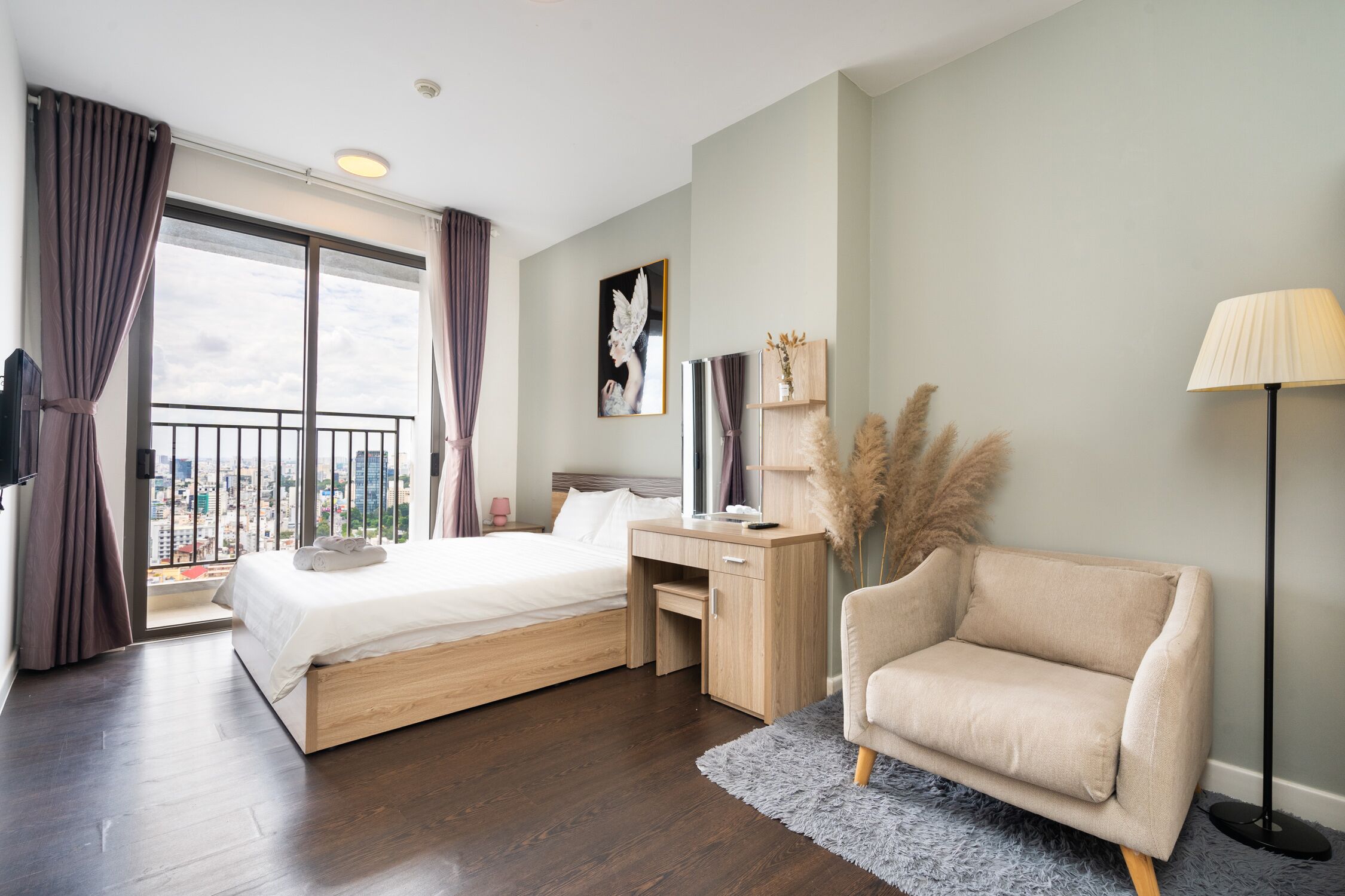 Habitación de hotel moderna con una cama grande, un escritorio, una silla y vistas a la ciudad desde un balcón.