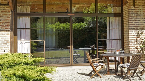 Ein Patio mit einem Holztisch und -stühlen, eine große Schiebetür zum Garten und eine Backsteinmauer.