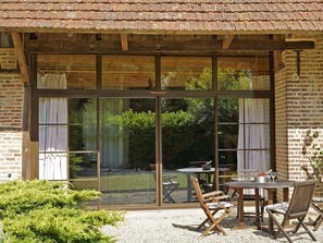 A patio area with a wooden table and chairs, a large sliding glass door leading to a garden, and a brick wall.