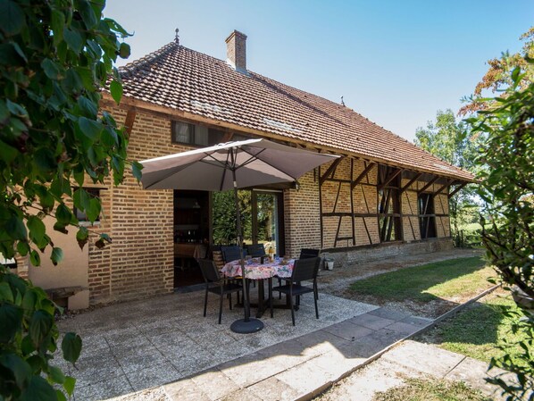 A brick house with a tiled roof, a covered patio with a table and chairs, and a gravel pathway.