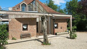 Ein zweistöckiges Haus mit Backsteinfassade und einem Balkon im oberen Geschoss, sowie einer Auffahrt mit Kies.